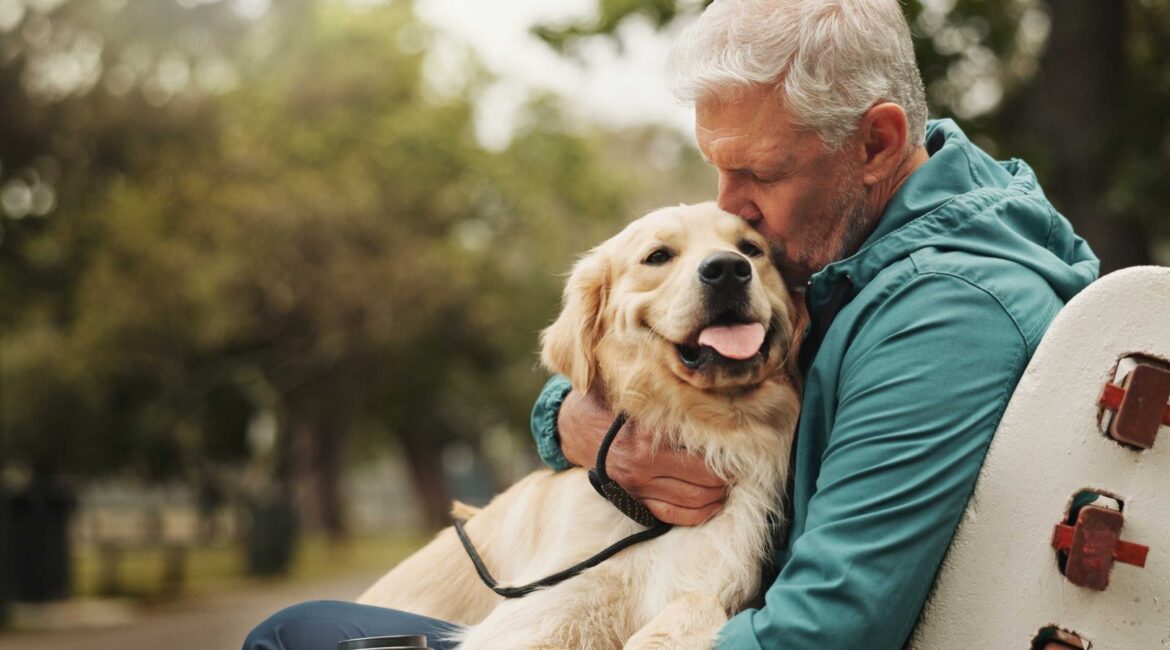 Hombre mayor abrazando a un golden retriever en un parque